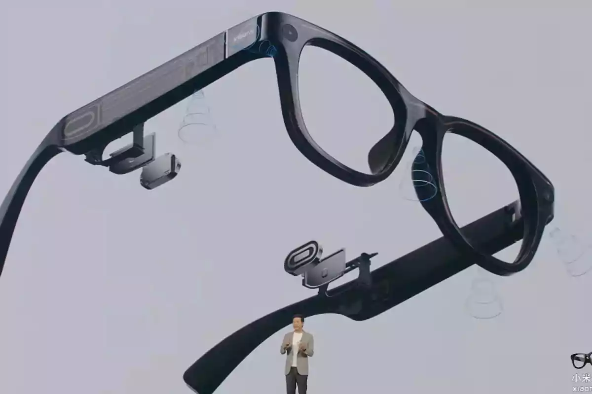Un hombre de pie presenta unas gafas inteligentes con componentes electrónicos visibles en una pantalla grande detrás de él Un hombre de pie presenta unas gafas inteligentes con componentes electrónicos visibles en una pantalla grande detrás de él