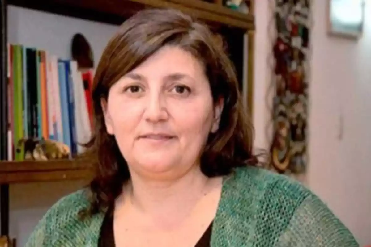 Mujer de cabello castaño y suelto con suéter verde posando frente a una estantería con libros Mujer de cabello castaño y suelto con suéter verde posando frente a una estantería con libros