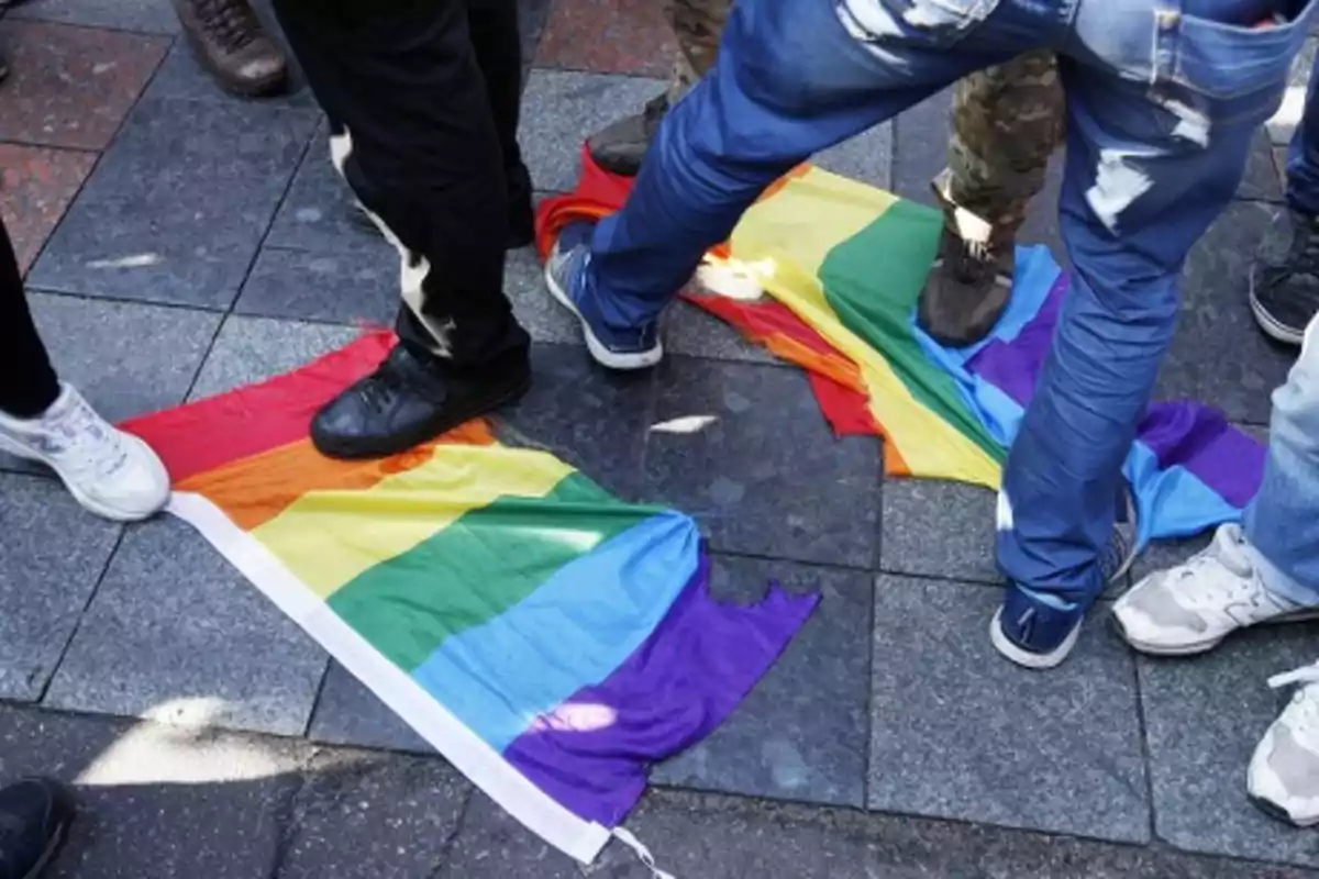 Several people step on LGBT pride flags on a sidewalk.