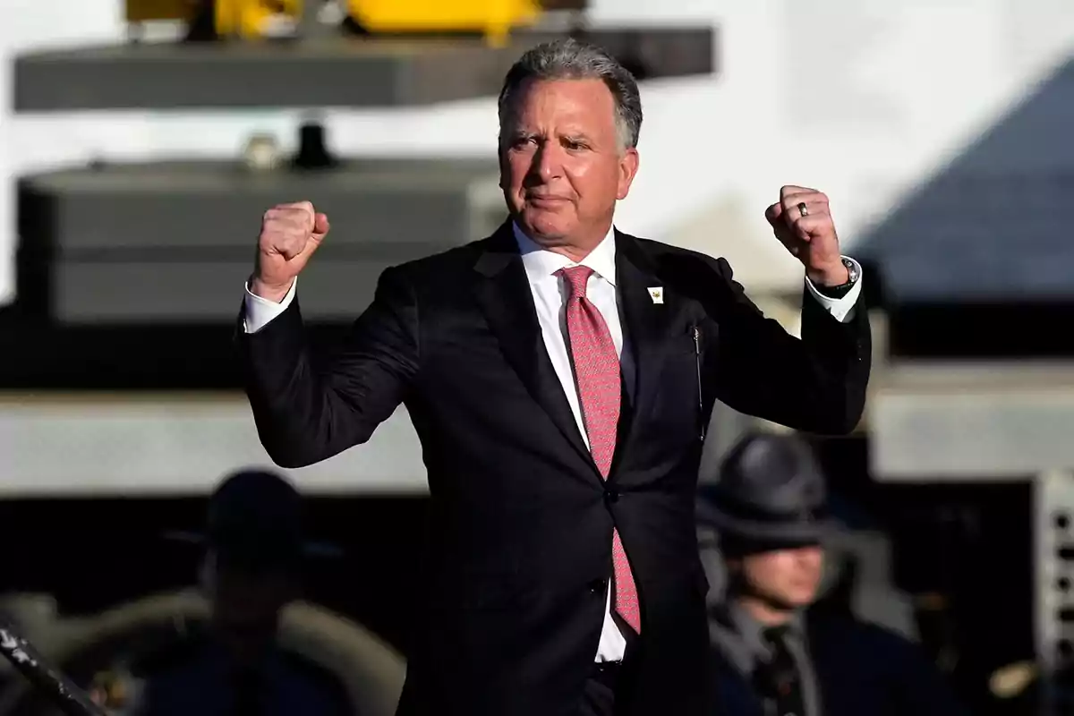 Man in a dark suit and red tie raising both fists in a gesture of triumph or celebration