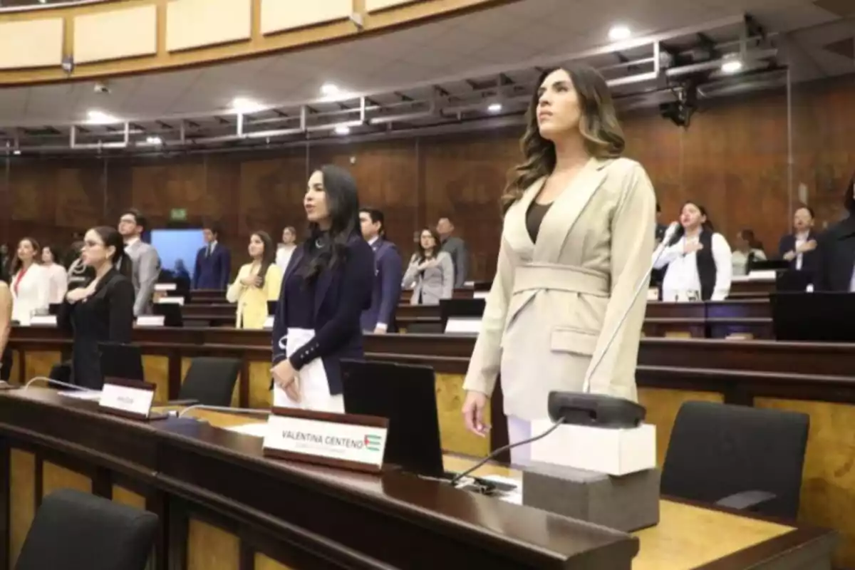 Varias personas de pie en un recinto parlamentario con la mano en el pecho durante una ceremonia oficial