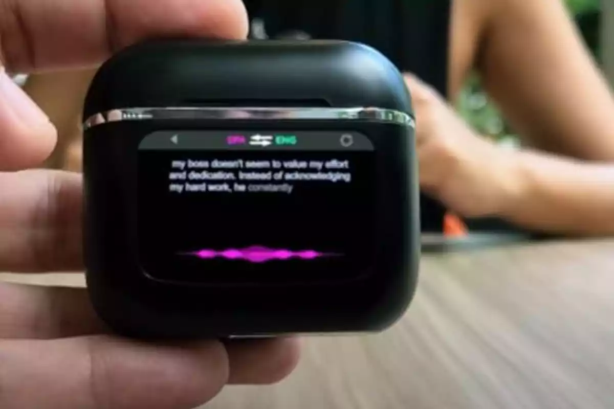 Persona sosteniendo un dispositivo de traducción portátil con pantalla que muestra texto en inglés y una onda de voz púrpura