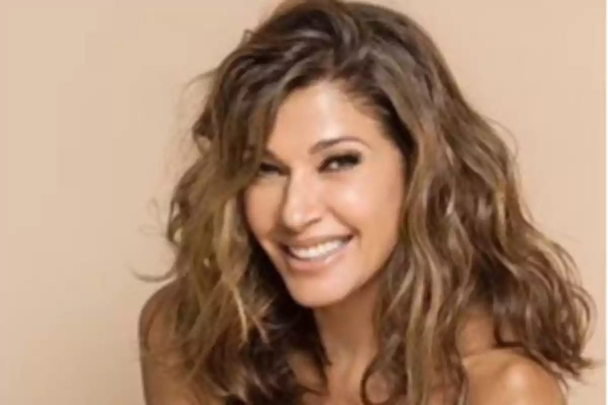 Woman with wavy brown hair smiling in front of a beige background