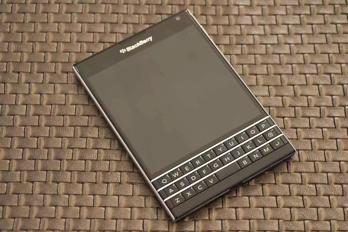 Teléfono BlackBerry con teclado físico sobre una superficie tejida marrón Teléfono BlackBerry con teclado físico sobre una superficie tejida marrón