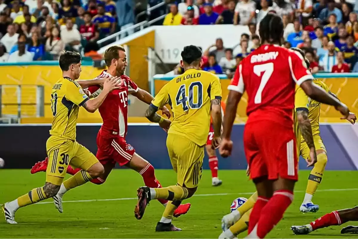 Jugadores de dos equipos de fútbol compiten por el balón en un partido con público en las gradas Jugadores de dos equipos de fútbol compiten por el balón en un partido con público en las gradas