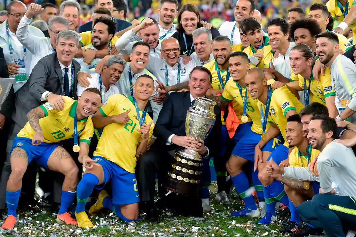 Jugadores y cuerpo técnico de la selección de fútbol de Brasil celebran sonrientes con medallas y un trofeo tras ganar un campeonato Jugadores y cuerpo técnico de la selección de fútbol de Brasil celebran sonrientes con medallas y un trofeo tras ganar un campeonato