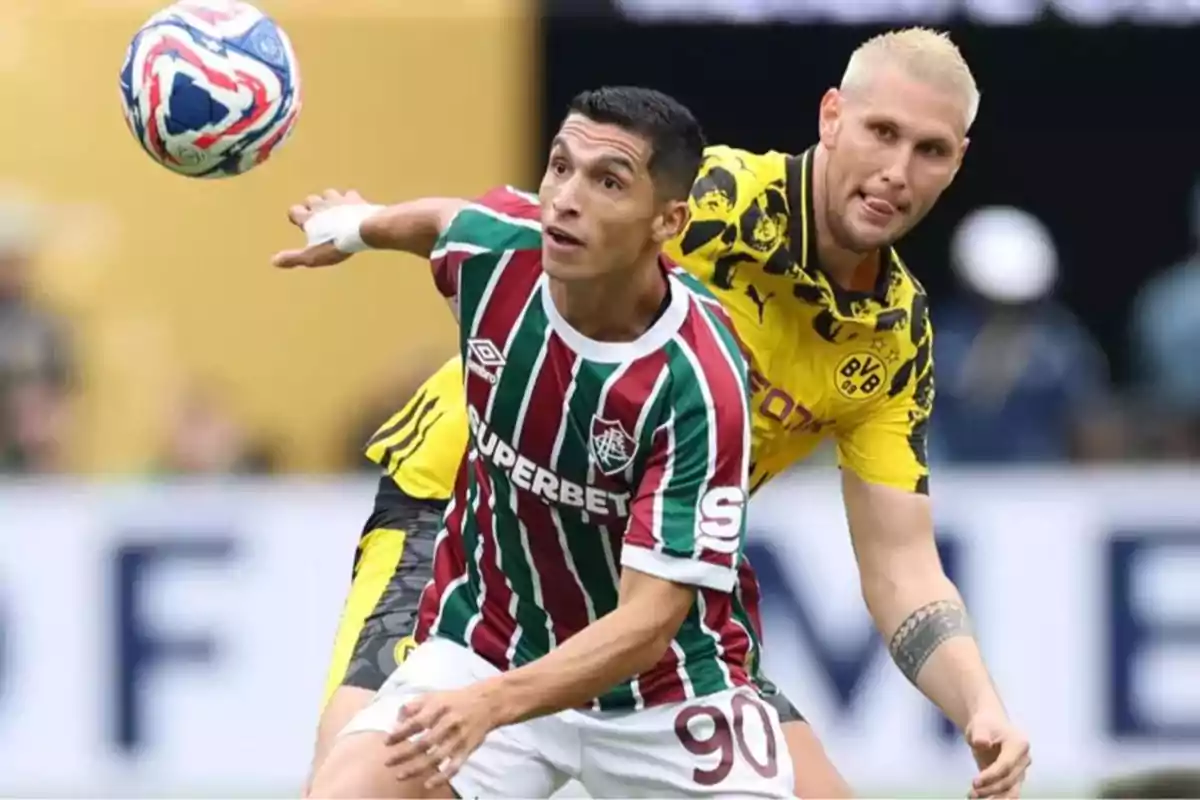 Two players compete for the ball during a match, one wearing a green, red, and white striped uniform and the other wearing a yellow and black uniform.