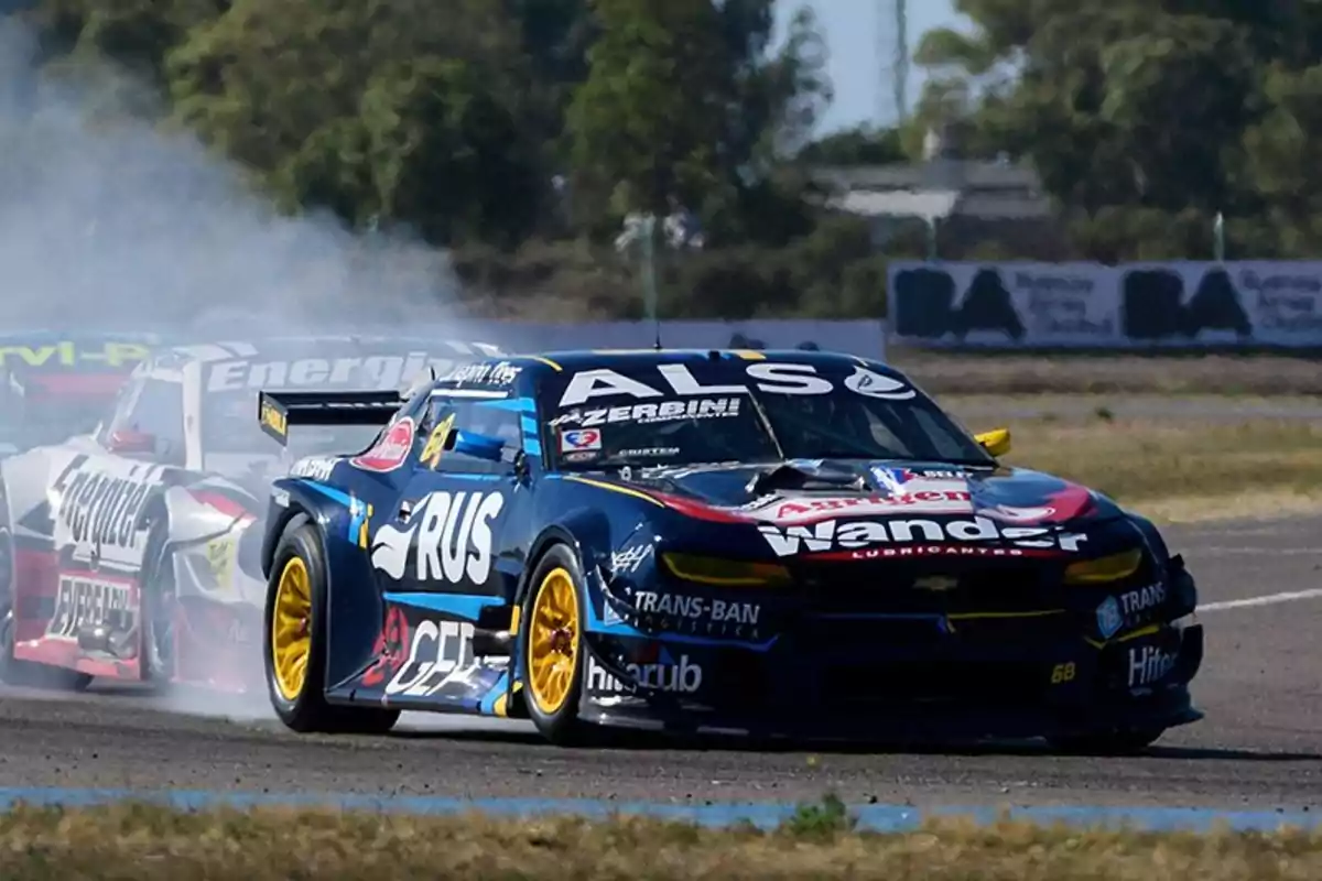 Autos de carrera compitiendo en una pista con humo saliendo de los neumáticos mientras toman una curva Autos de carrera compitiendo en una pista con humo saliendo de los neumáticos mientras toman una curva