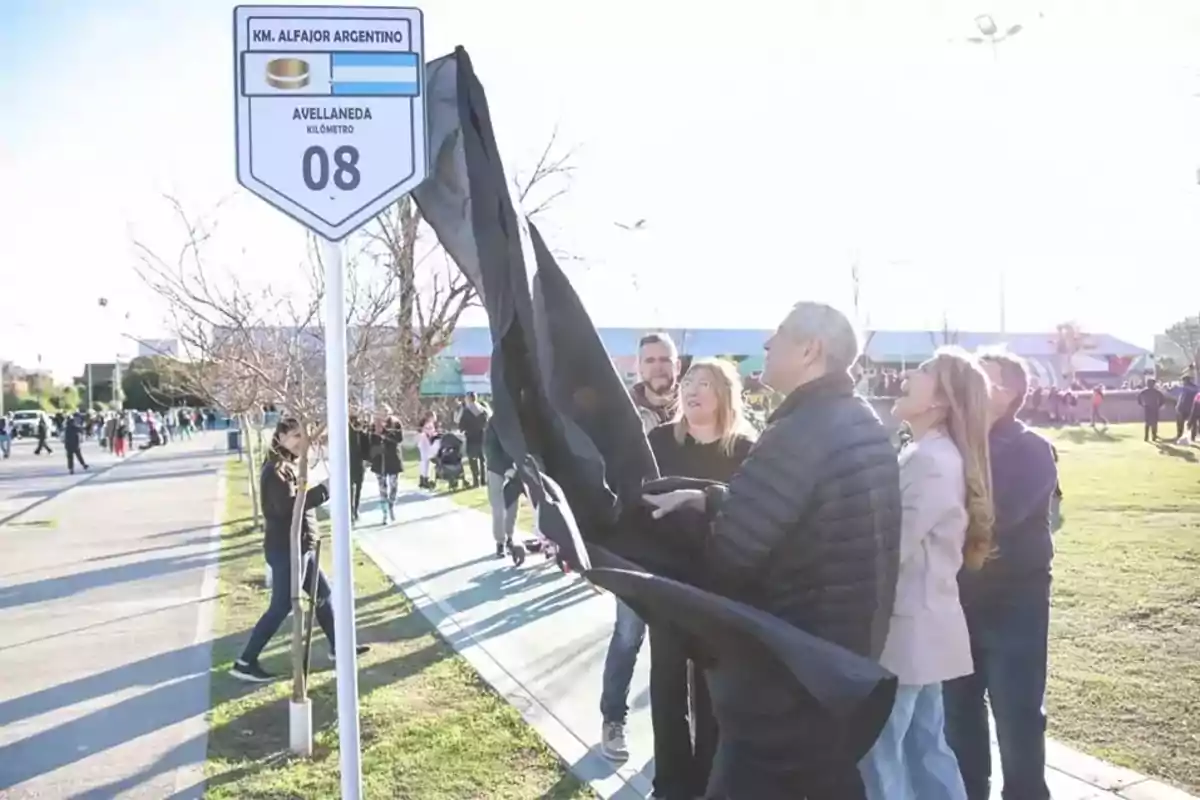 A group of people discovers a sign that marks the Argentine alfajor kilometer in Avellaneda during an outdoor event. A group of people discovers a sign that marks the Argentine alfajor kilometer in Avellaneda during an outdoor event.