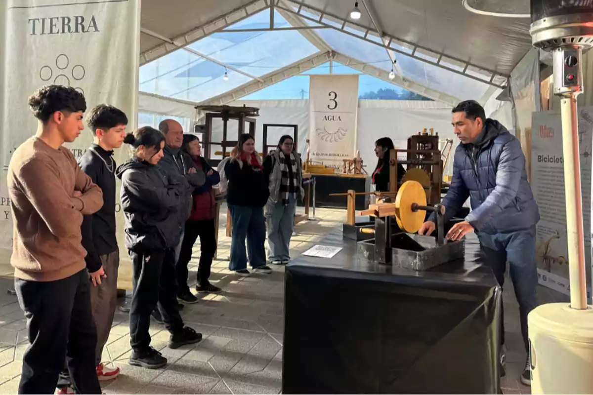 Un grupo de personas observa atentamente una demostración de una máquina antigua en una exposición bajo una carpa iluminada