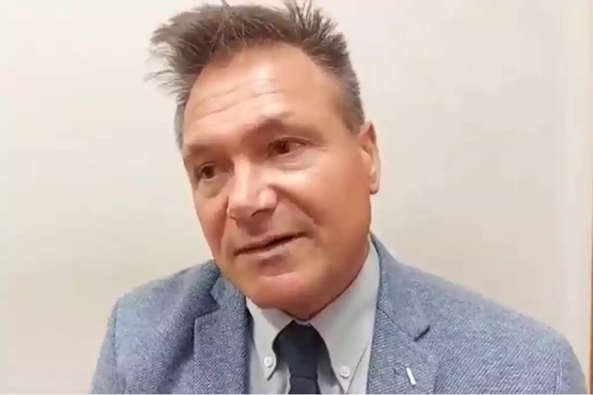 Middle-aged man in a light blue jacket and dark tie looking to the side in front of a light-colored wall Middle-aged man in a light blue jacket and dark tie looking to the side in front of a light-colored wall