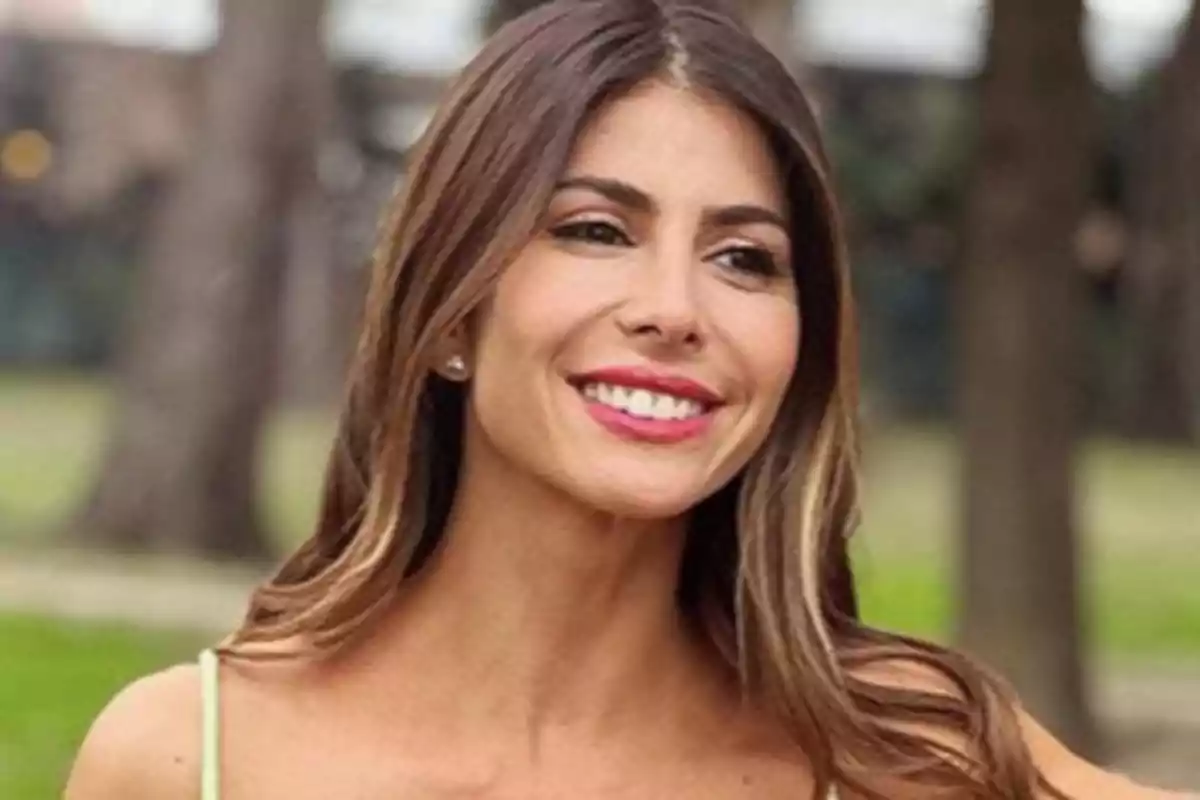 Mujer joven de cabello largo y castaño sonriendo al aire libre con árboles de fondo Mujer joven de cabello largo y castaño sonriendo al aire libre con árboles de fondo