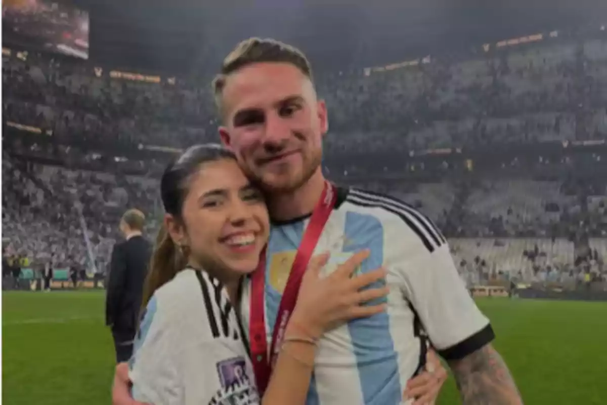 Pareja abrazada en un estadio de fútbol con camisetas de la selección argentina y medalla