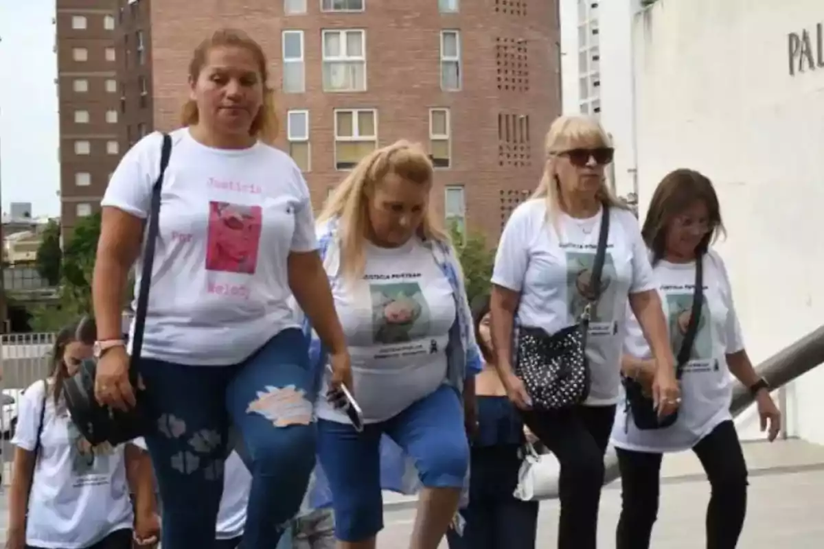 A group of women wearing white t-jerseys with messages of justice and printed photos walks up some stairs in a city.