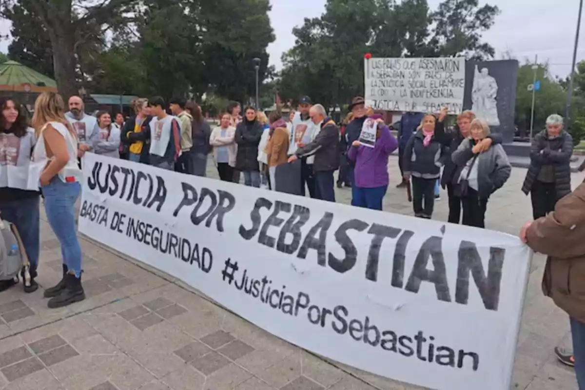Un grupo de personas se manifiesta en la vía pública sosteniendo una pancarta que exige justicia por Sebastián y reclama el fin de la inseguridad, mientras otras personas observan y muestran carteles relacionados con la causa.