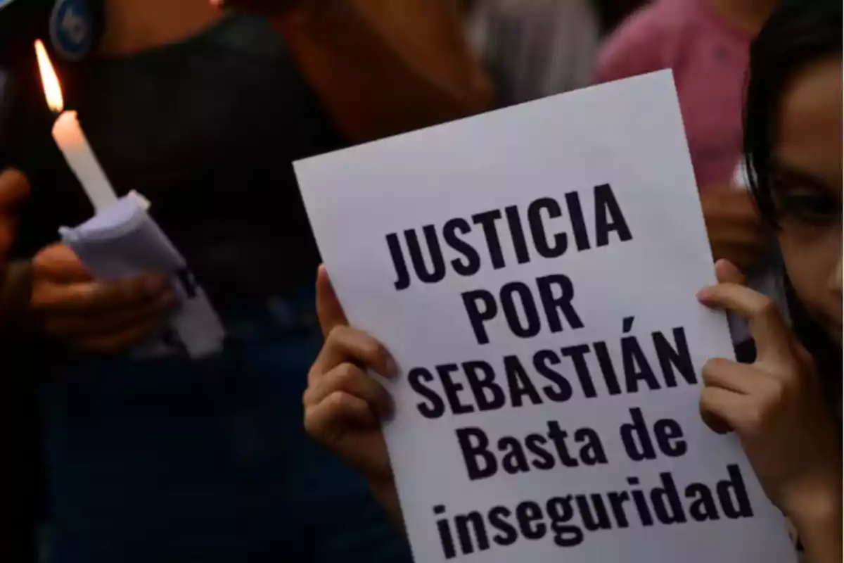 Persona sostiene un cartel que dice justicia por Sebastián basta de inseguridad mientras otra persona sostiene una vela encendida Persona sostiene un cartel que dice justicia por Sebastián basta de inseguridad mientras otra persona sostiene una vela encendida