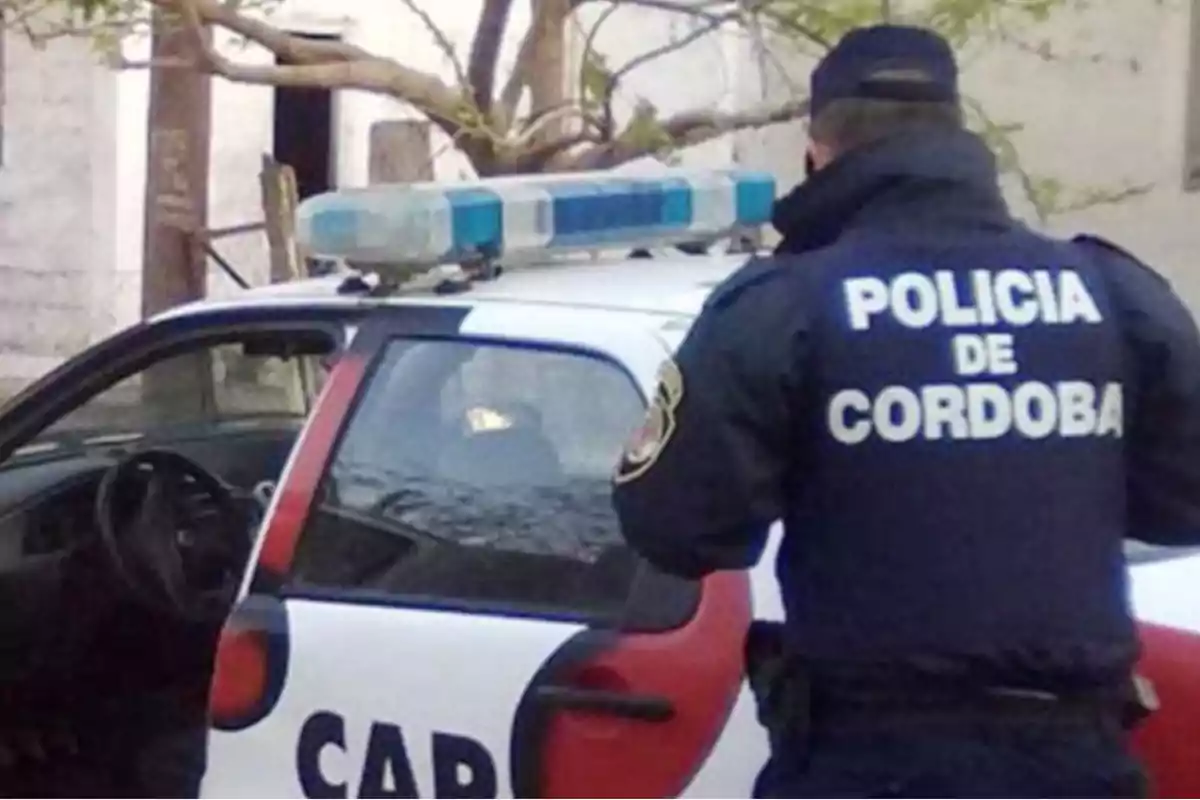 Un policía de Córdoba de espaldas junto a un patrullero estacionado Un policía de Córdoba de espaldas junto a un patrullero estacionado