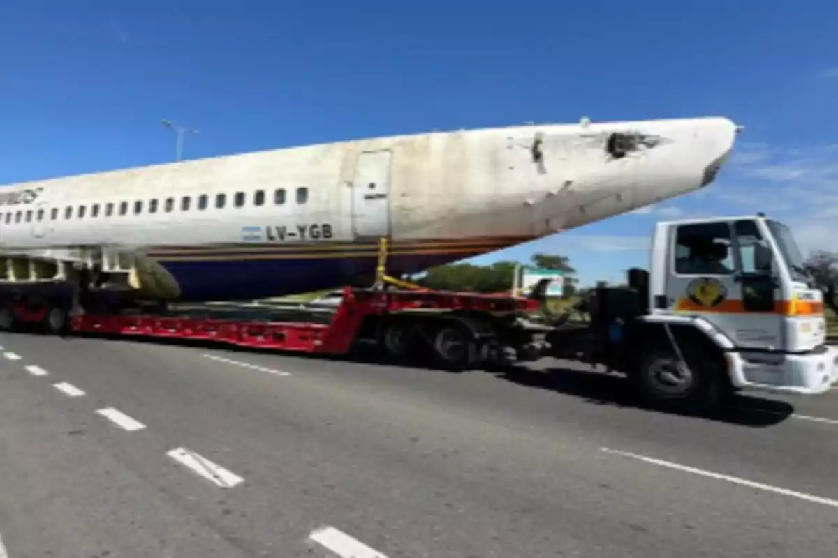 A truck is transporting an airplane fuselage on a highway on a sunny day.