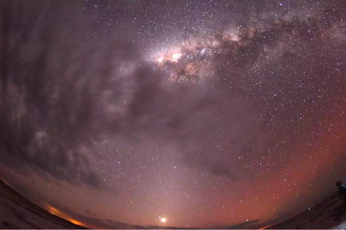 Cielo nocturno con la Vía Láctea visible entre nubes y un resplandor en el horizonte Cielo nocturno con la Vía Láctea visible entre nubes y un resplandor en el horizonte