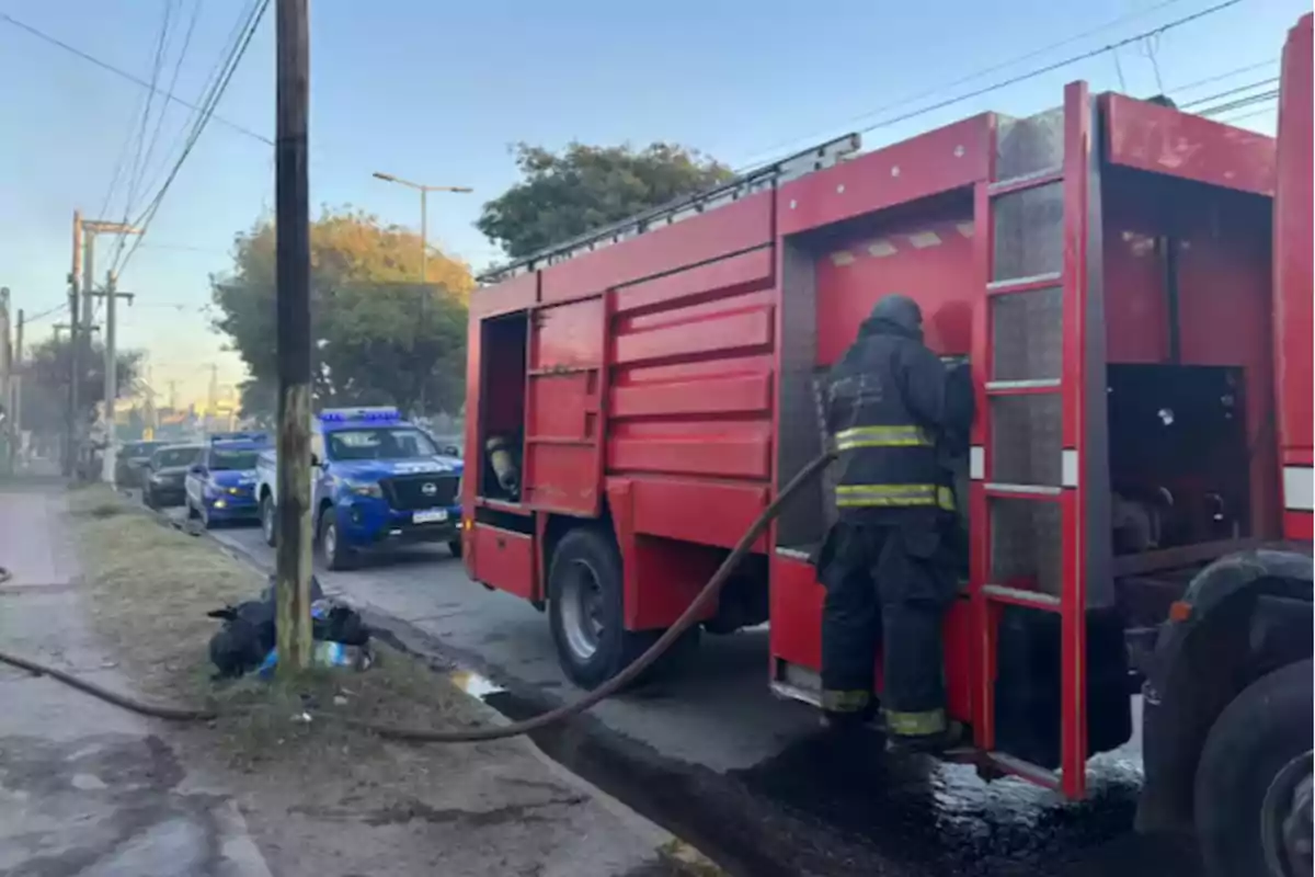 Un bombero trabaja junto a un camión de bomberos rojo mientras varias patrullas de policía están estacionadas en la calle