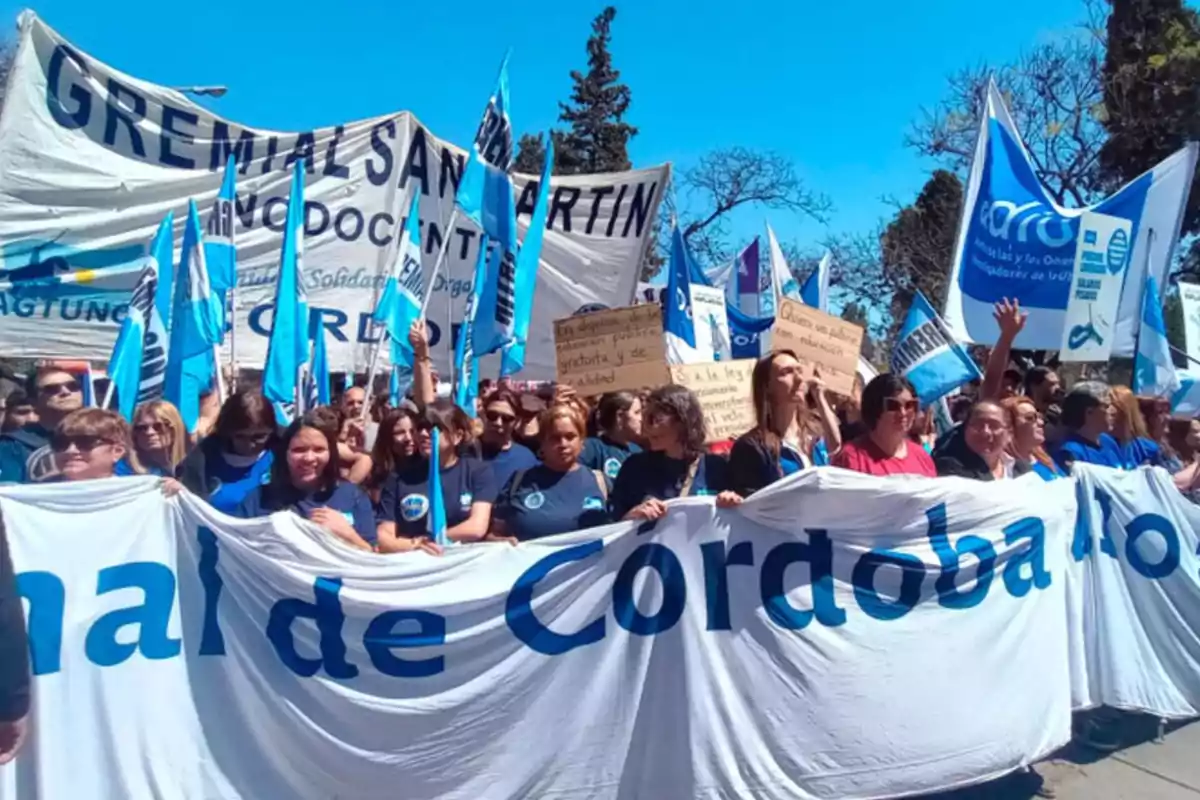 Un grupo de personas marcha en la calle sosteniendo pancartas y banderas azules y blancas en una manifestación gremial en Córdoba Un grupo de personas marcha en la calle sosteniendo pancartas y banderas azules y blancas en una manifestación gremial en Córdoba
