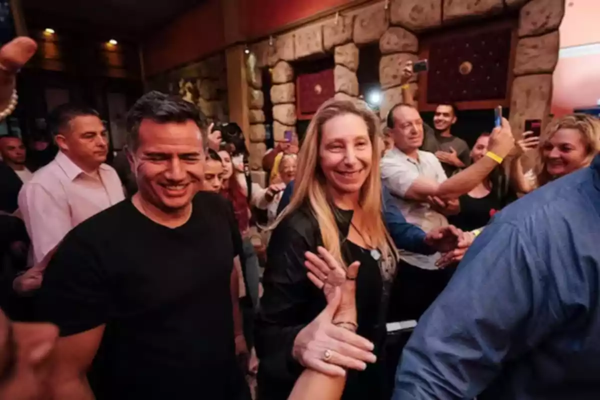 Un grupo de personas sonríe y saluda mientras camina entre una multitud en un ambiente festivo y animado Un grupo de personas sonríe y saluda mientras camina entre una multitud en un ambiente festivo y animado