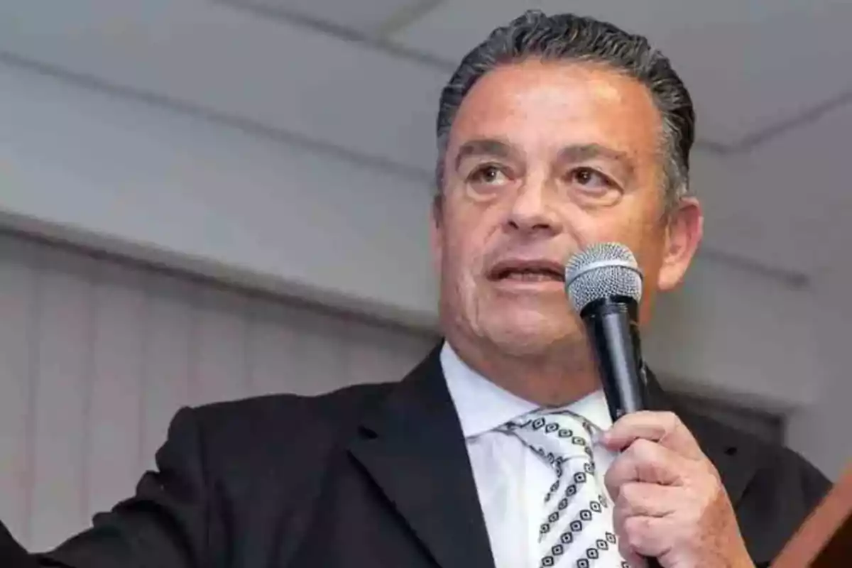 Man in a suit and tie speaking into a microphone at an indoor event Man in a suit and tie speaking into a microphone at an indoor event