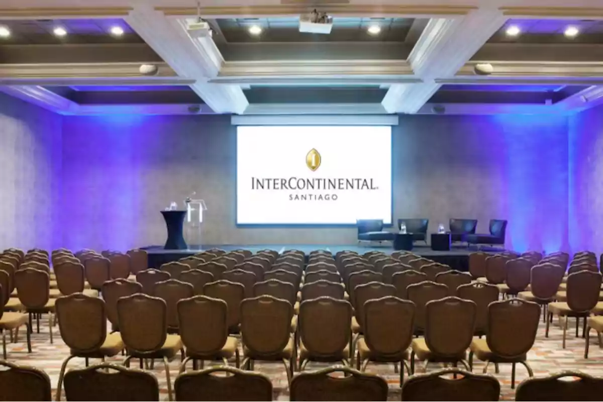 Salón de conferencias con filas de sillas vacías frente a un escenario con pantalla grande y luces azules en el hotel InterContinental Santiago
