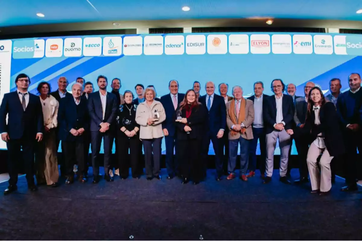 Group of people posing on a stage during a corporate event with a background screen displaying sponsor company logos