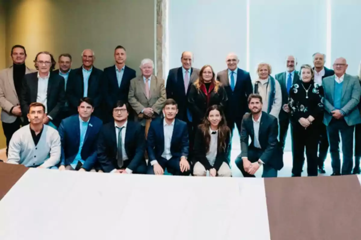 A group of people posing for a formal photo indoors with a light background and a table in front. A group of people posing for a formal photo indoors with a light background and a table in front.