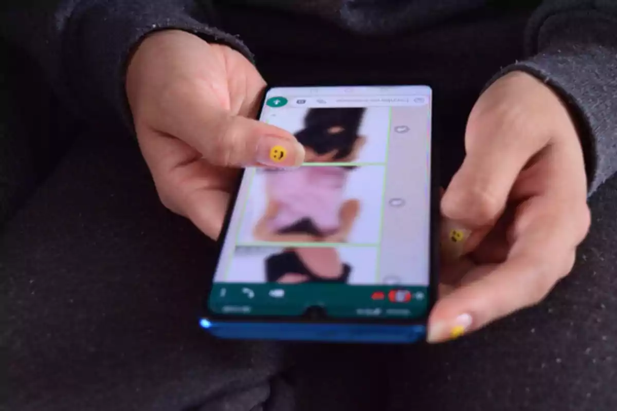 Person holding a mobile phone with blurry images on the screen and nails decorated with smiley faces