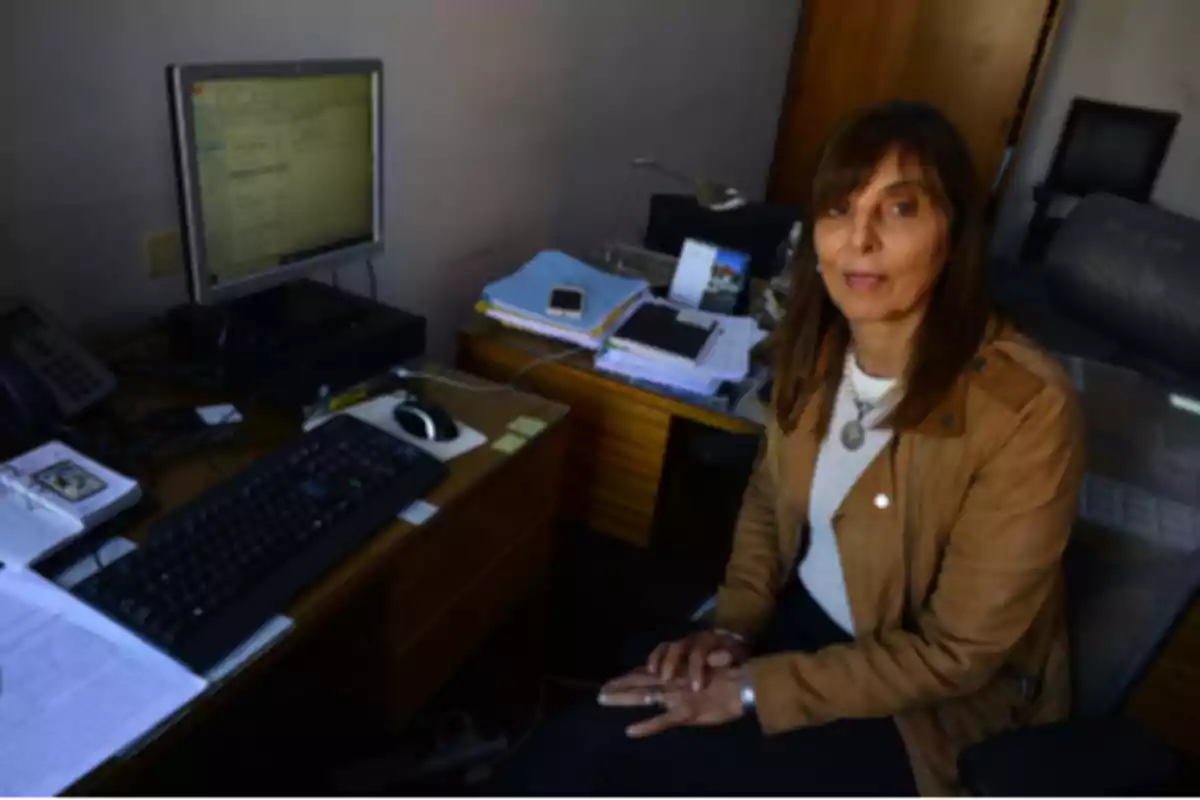 Woman sitting in an office next to a desk with a computer, keyboard, documents, and phone Woman sitting in an office next to a desk with a computer, keyboard, documents, and phone