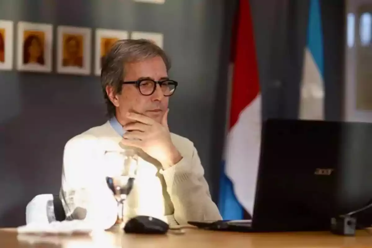 Gray-haired man with glasses sitting in front of a laptop with a thoughtful expression in a sunlit office Gray-haired man with glasses sitting in front of a laptop with a thoughtful expression in a sunlit office