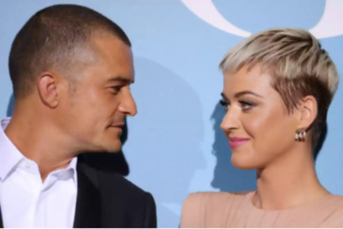 Un hombre y una mujer se miran sonrientes frente a un fondo azul Un hombre y una mujer se miran sonrientes frente a un fondo azul
