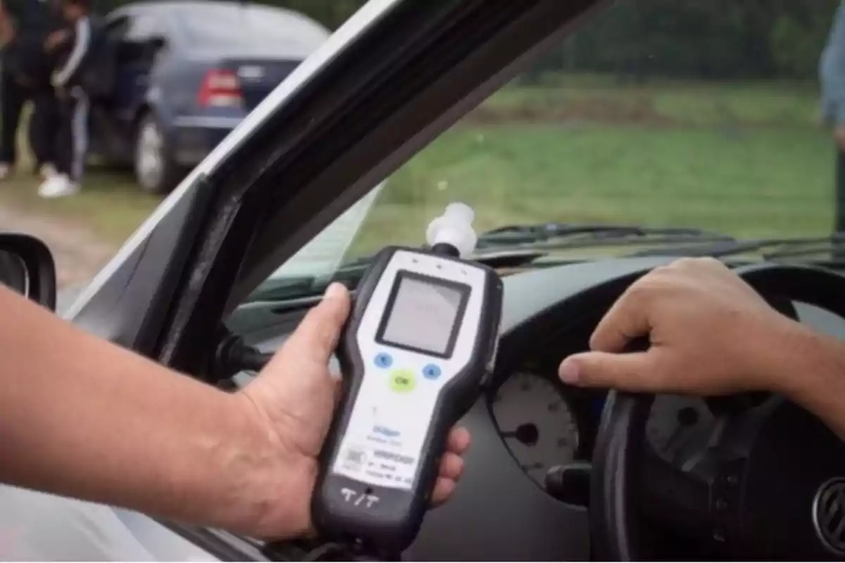 Person holding a breathalyzer in front of a driver inside a car