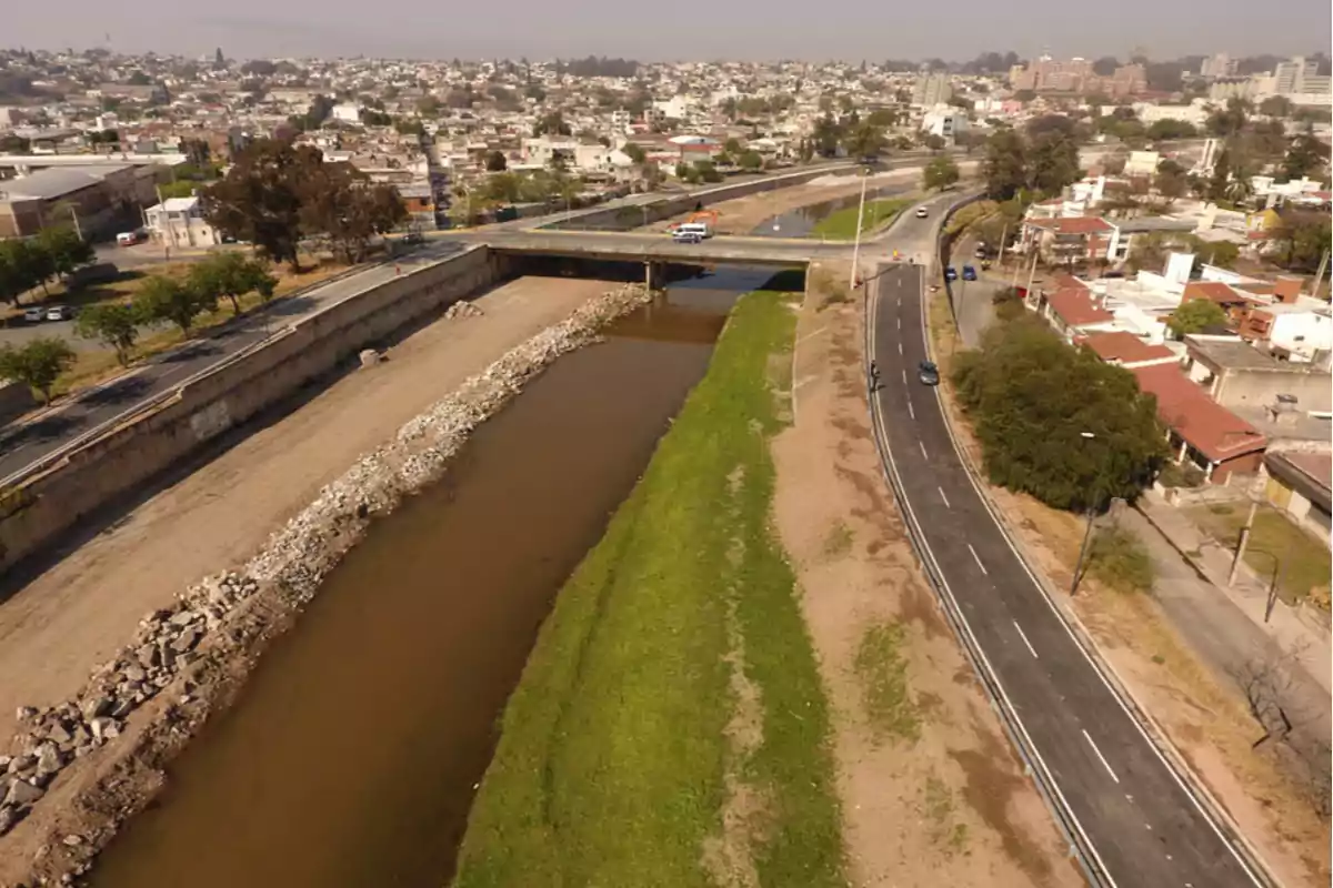 Vista aérea de un río con agua marrón, un puente vehicular y una carretera asfaltada junto a una zona residencial en una ciudad