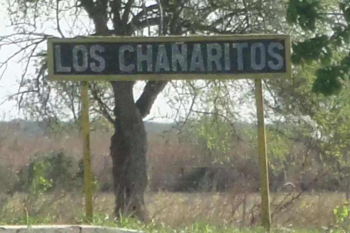 Welcome sign to Los Chañaritos in a rural setting with trees and dry grass in the background