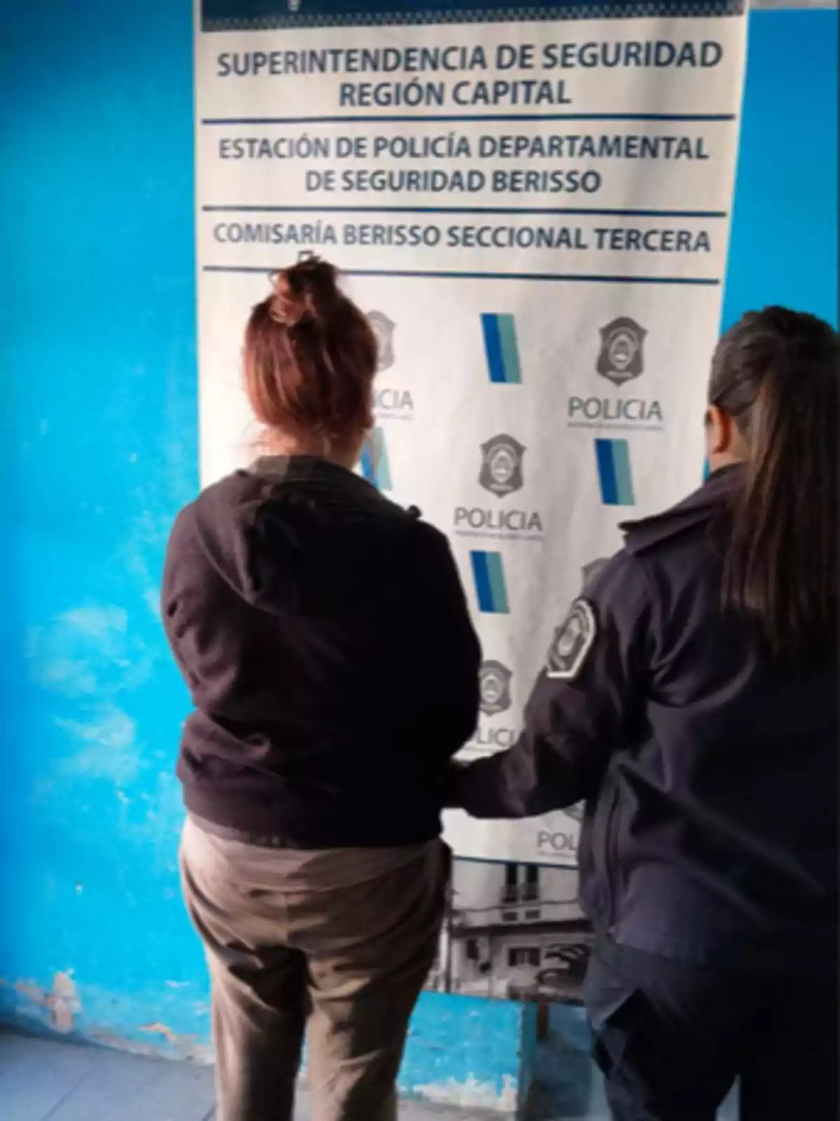 Dos mujeres de espaldas frente a un cartel policial en una comisaría Dos mujeres de espaldas frente a un cartel policial en una comisaría
