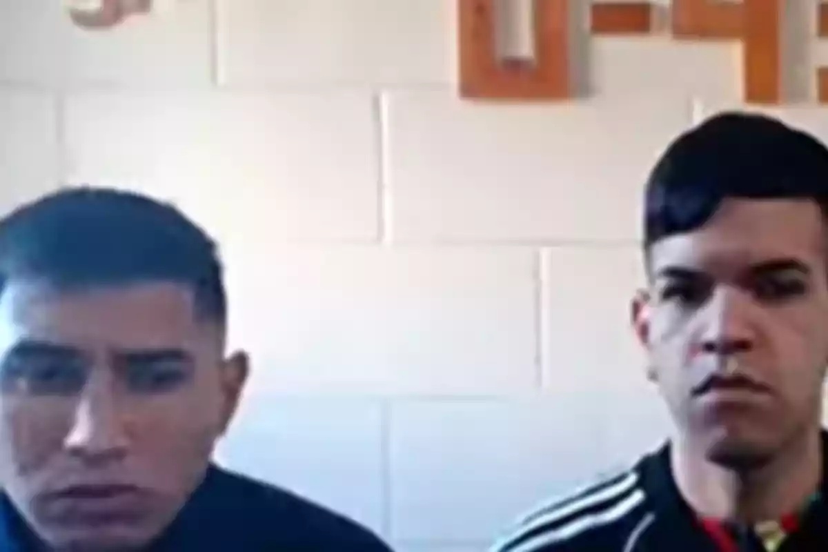 Two young men with serious expressions are sitting next to each other in front of a white wall. Two young men with serious expressions are sitting next to each other in front of a white wall.