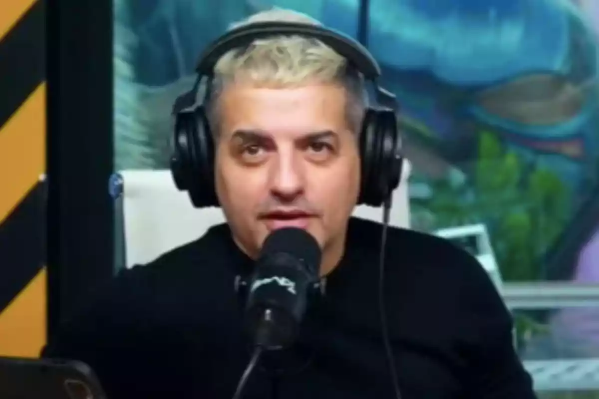 Hombre de cabello corto y rubio usando audífonos grandes y hablando frente a un micrófono en un estudio de grabación