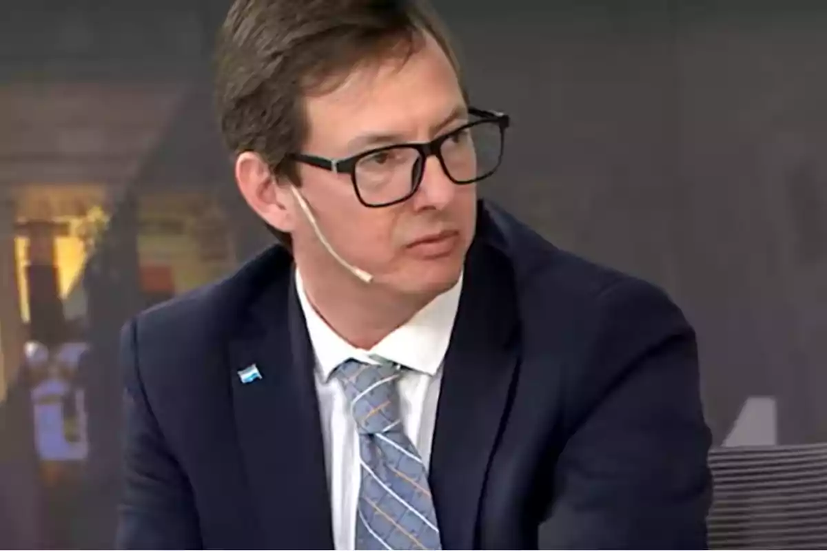 Hombre con gafas y traje azul usando micrófono de diadema en un estudio de televisión