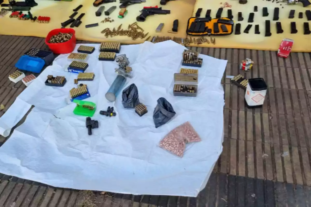 Diversos cartuchos, municiones y cargadores de armas de fuego organizados sobre mantas blancas y amarillas en el suelo