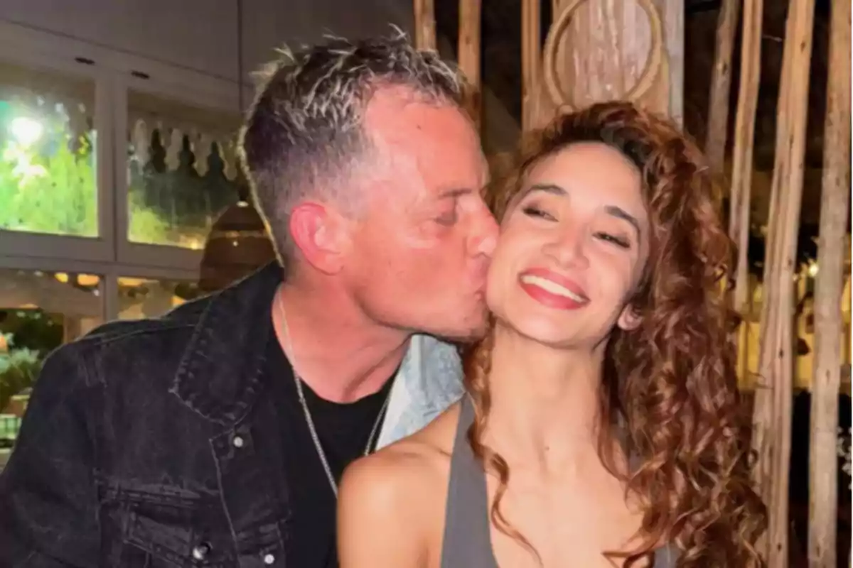 Hombre besando en la mejilla a una mujer sonriente en un ambiente interior cálido Hombre besando en la mejilla a una mujer sonriente en un ambiente interior cálido