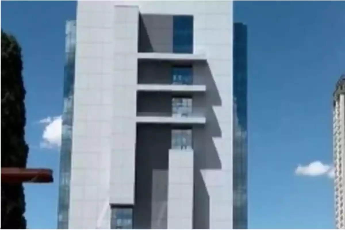 Edificio moderno de varios pisos con una fachada blanca y ventanales azules bajo un cielo despejado Edificio moderno de varios pisos con una fachada blanca y ventanales azules bajo un cielo despejado