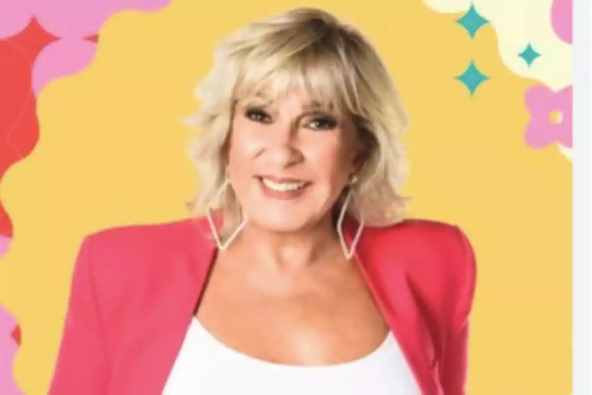 Mujer rubia con cabello corto y ondulado, usando un saco rosa y blusa blanca, sonríe frente a un fondo colorido con formas y flores.
