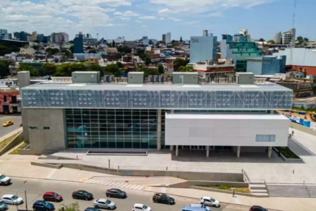 Modern multi-story building with a glass and concrete facade located in a city, with cars parked in front and buildings in the background Modern multi-story building with a glass and concrete facade located in a city, with cars parked in front and buildings in the background