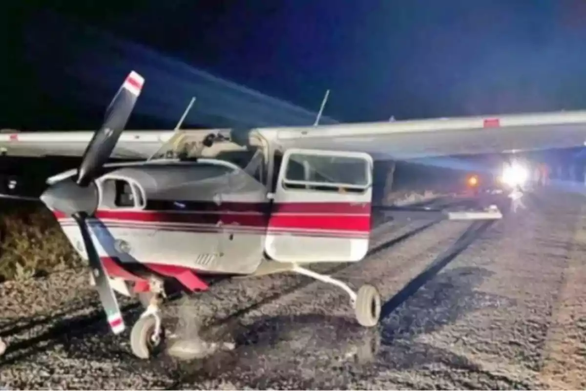 Avioneta pequeña con rayas rojas y blancas detenida en una carretera de noche con la puerta abierta y luces al fondo Avioneta pequeña con rayas rojas y blancas detenida en una carretera de noche con la puerta abierta y luces al fondo