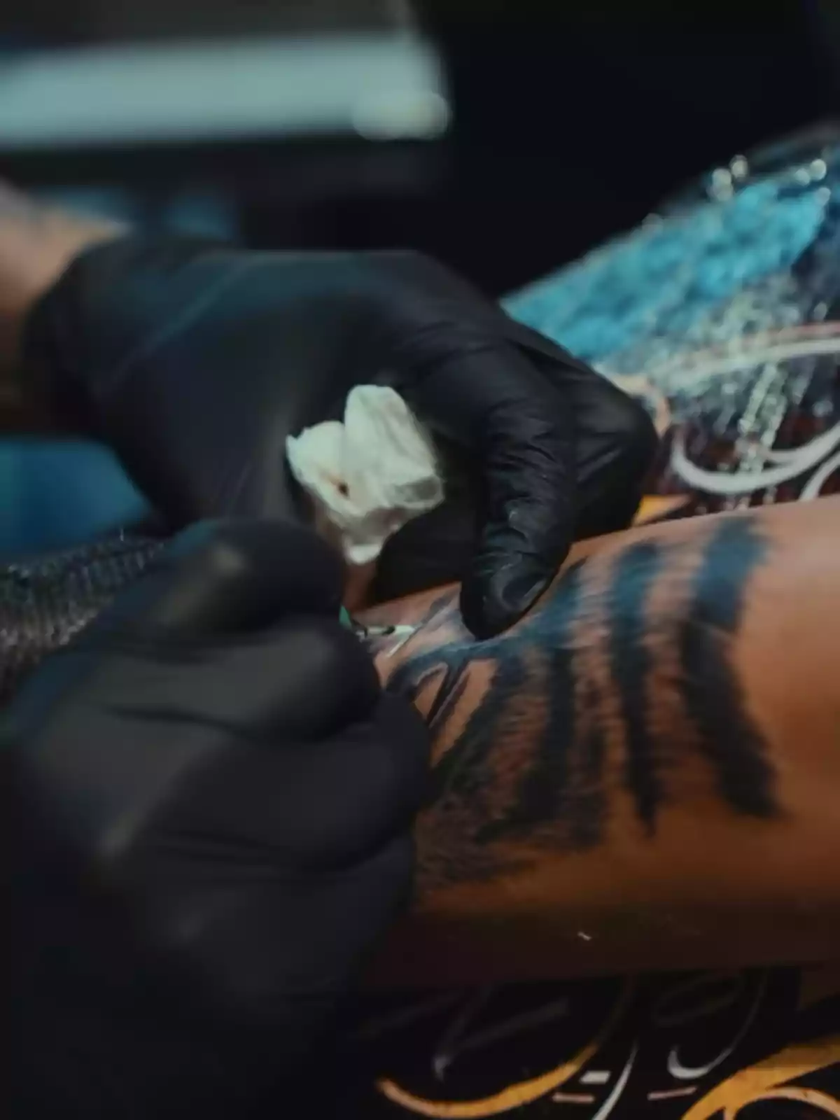 Hand with a black glove tattooing a dark design on a person's arm Hand with a black glove tattooing a dark design on a person's arm