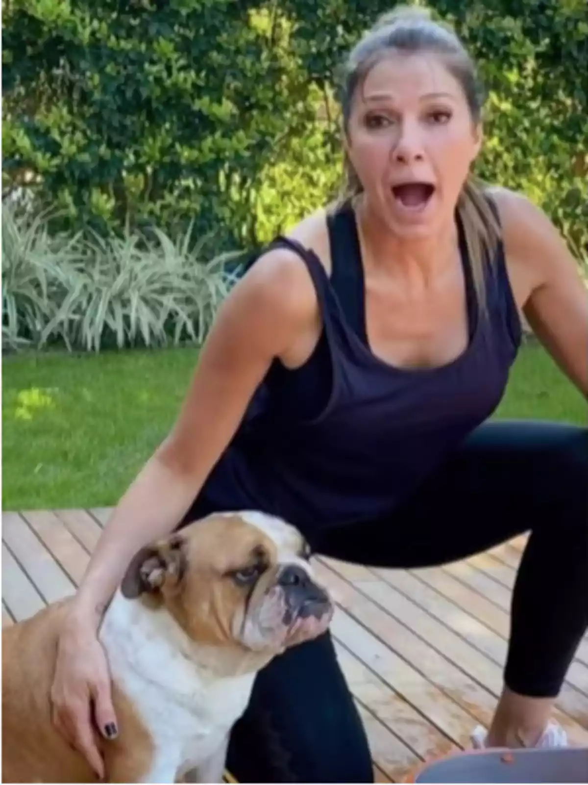Surprised woman in sportswear petting a bulldog in a garden Surprised woman in sportswear petting a bulldog in a garden
