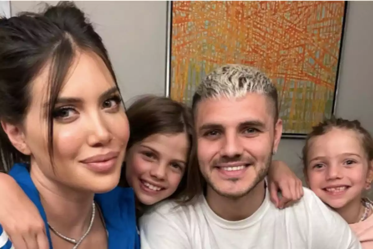 A woman and a man smile alongside two little girls, all hugging and posing for a selfie in front of a colorful painting.